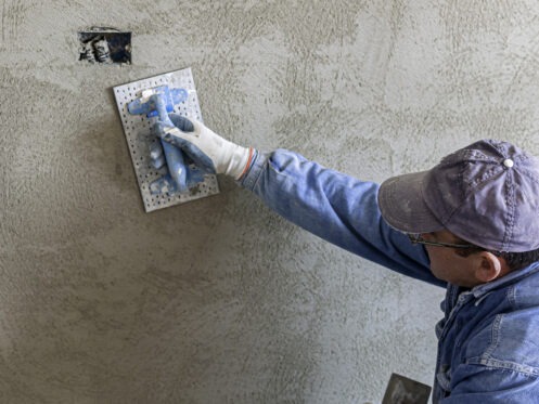 A worker smoothing a stucco patch on a gray wall with a float